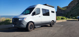 An RV rental, a white Mercedes Sprinter van, parked at a scenic viewpoint overlooking a valley and rock formations.