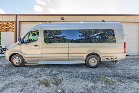Silver Mercedes-Benz Sprinter RV rental van with tinted windows, parked on gravel outside a building. Perfect for your next adventure.