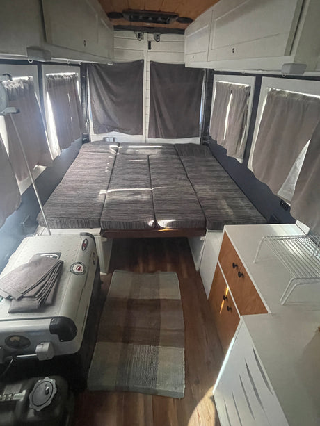 RV rental interior: Cozy camper van featuring a large modular bed, overhead storage, side curtains, and compact living amenities.