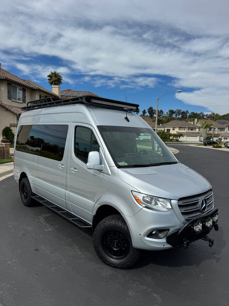 Silver Mercedes Sprinter adventure van, customized with roof rack and off-road tires, ready for your next RV rental journey.