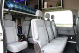 View of an RV rental's versatile interior, showing comfortable grey passenger seating, an overhead bunk, and storage.