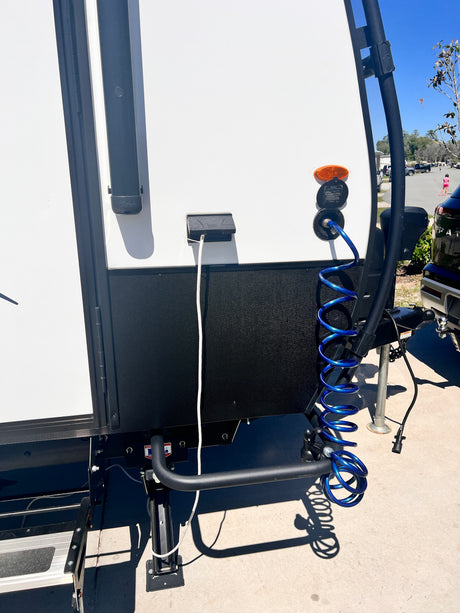 Side view of an RV rental at a campground. Power cable & blue coiled water hose are connected for setup.