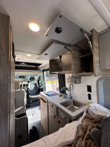 RV rental interior featuring a compact kitchenette, cozy bed, and front cabin view for comfortable travel.