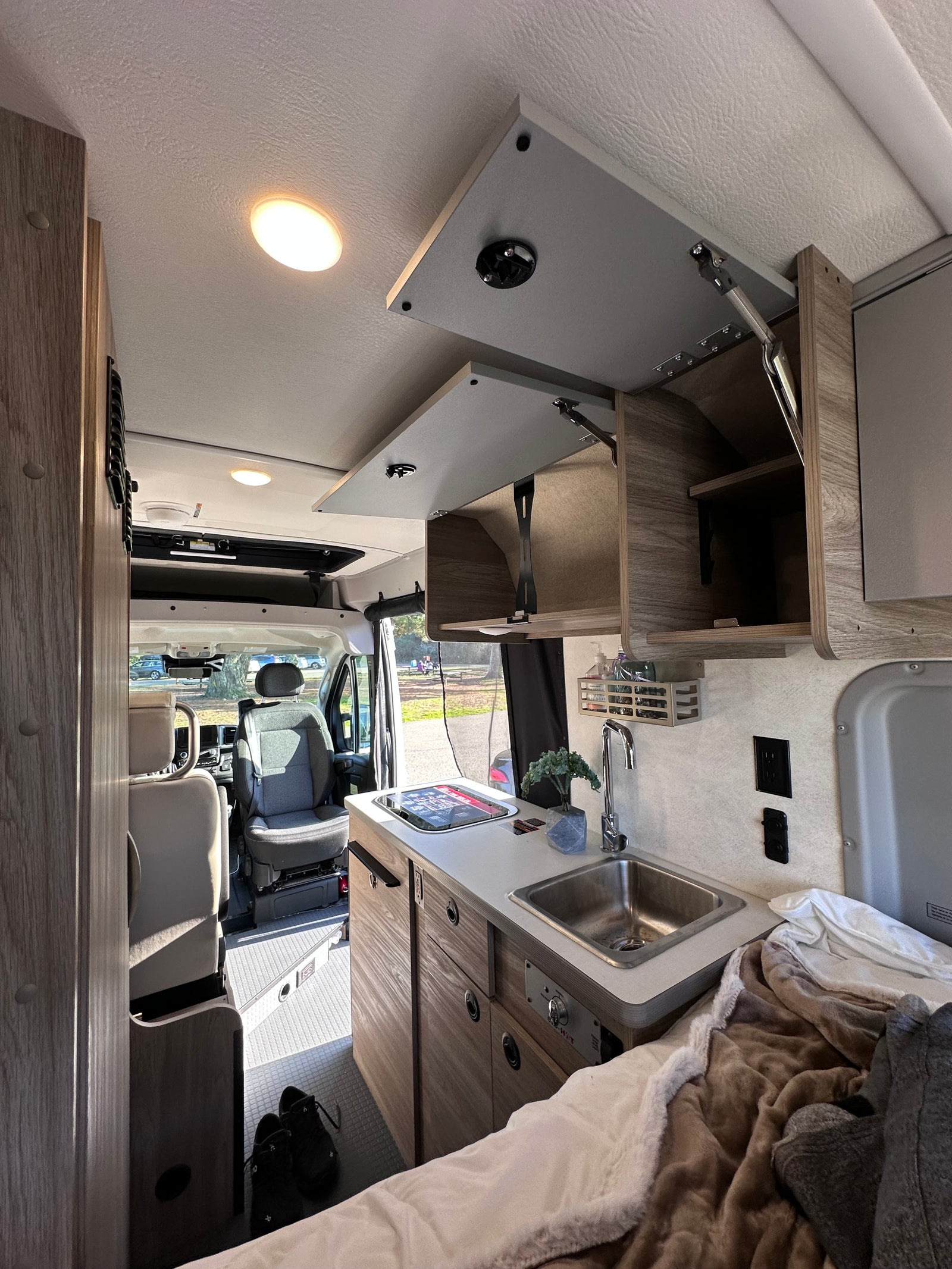 RV rental interior featuring a compact kitchenette, cozy bed, and front cabin view for comfortable travel.