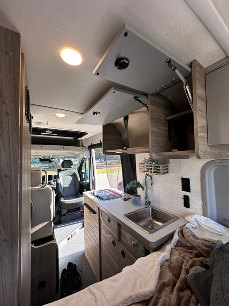 RV rental interior featuring a compact kitchenette, cozy bed, and front cabin view for comfortable travel.