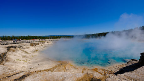Explore Yellowstone's steaming blue thermal pool and boardwalk with an RV rental. Tourists enjoy the unique natural beauty.