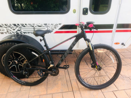 Black & pink Trek mountain bike parked beside a white RV rental. Ready for trail adventures & travel.