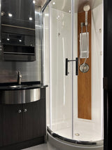 Modern RV rental bathroom: a sleek vanity with sink, clear glass shower, and wood accent panel. Compact, stylish, and ready for travel.