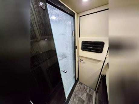 RV rental: Modern shower interior with clear and textured glass door, cream walls, and wood-look floor.
