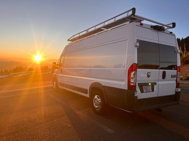 White RV rental van parked at a mountain overlook under a stunning orange sunset, perfect for a road trip adventure.