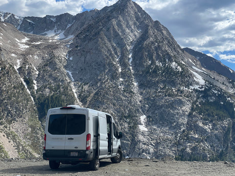 Adventure awaits! This white RV rental is parked among stunning, snow-capped mountains under a cloudy sky.
