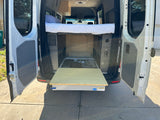 Inside an RV rental van: raised bed & pull-out table for flexible mobile living and camping.