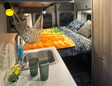 Cozy rv rental interior featuring a bed with vibrant bedding, a compact kitchen sink, and decorative hanging net lights.