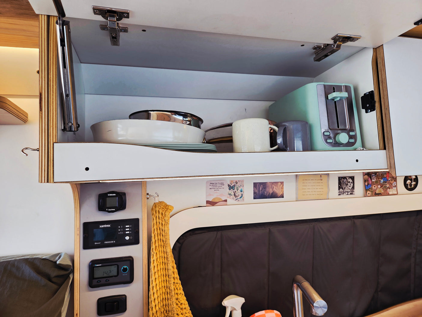 Cozy RV rental kitchenette with open cabinet, dishes, toaster, and control panel. Ready for your road trip!