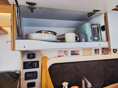 Cozy RV rental kitchenette with open cabinet, dishes, toaster, and control panel. Ready for your road trip!