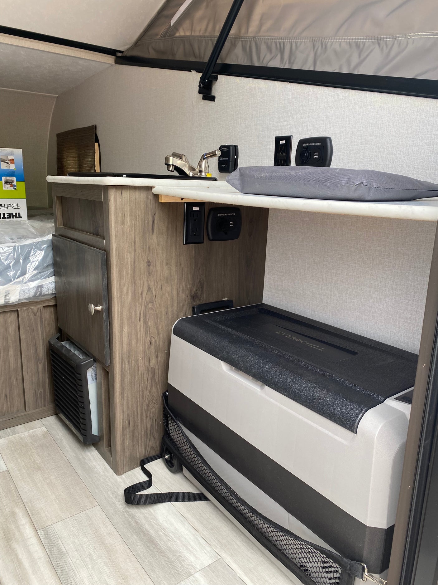 RV rental interior with kitchenette, sink, charging station, portable fridge, and heater unit near the sleeping area.