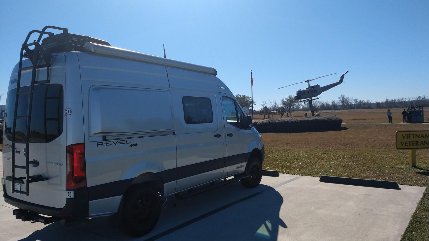 A Mercedes-Benz Sprinter RV rental van (Winnebago Revel 4x4) parked facing a Vietnam veteran helicopter memorial under a clear sky. — photo 2