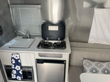View of an RV rental kitchen showing a compact sink, stove, microwave, and small fridge, with cozy seating adjacent.