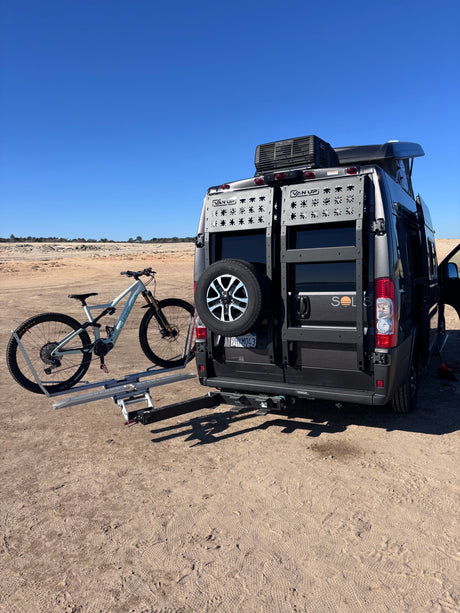 Solis RV rental van with a mountain bike on its rear rack, parked in a desert. Ideal for outdoor adventure!