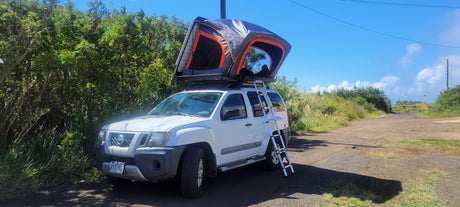 Experience nature with our RV rental! This white Nissan Xterra SUV with a rooftop tent and ladder is ready for adventure.