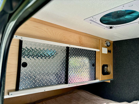Inside an RV rental: overhead diamond plate storage, wood trim, ceiling fan, outlets, and bed.