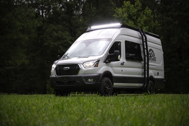 White Ford Transit camper van with bright roof lights & off-road tires, parked on grass. Ideal for your next rv rental adventure.
