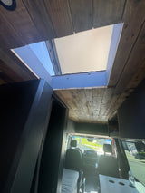 RV rental's custom interior: rustic wood ceiling, large skylight, and modern cabinetry leading to the driver's cabin.