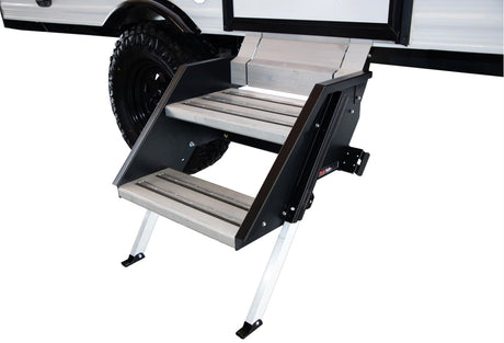 Sturdy, multi-level aluminum RV rental entry steps extended from a white camper with a rugged tire.