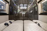Luxury RV rental: plush quilted beds with seatbelts, glossy wood walls, windows, and central TV offer travel comfort.