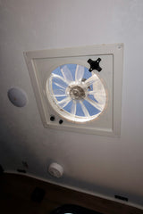 RV rental ceiling: a white vent fan with a screen open to the blue sky, offering fresh air for travel.