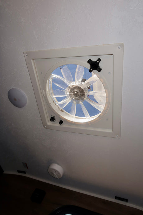 RV rental ceiling: a white vent fan with a screen open to the blue sky, offering fresh air for travel.