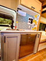 This RV rental features a modern kitchen with a sink, fridge, light-colored cabinets, and a scenic window view, perfect for van life adventures.