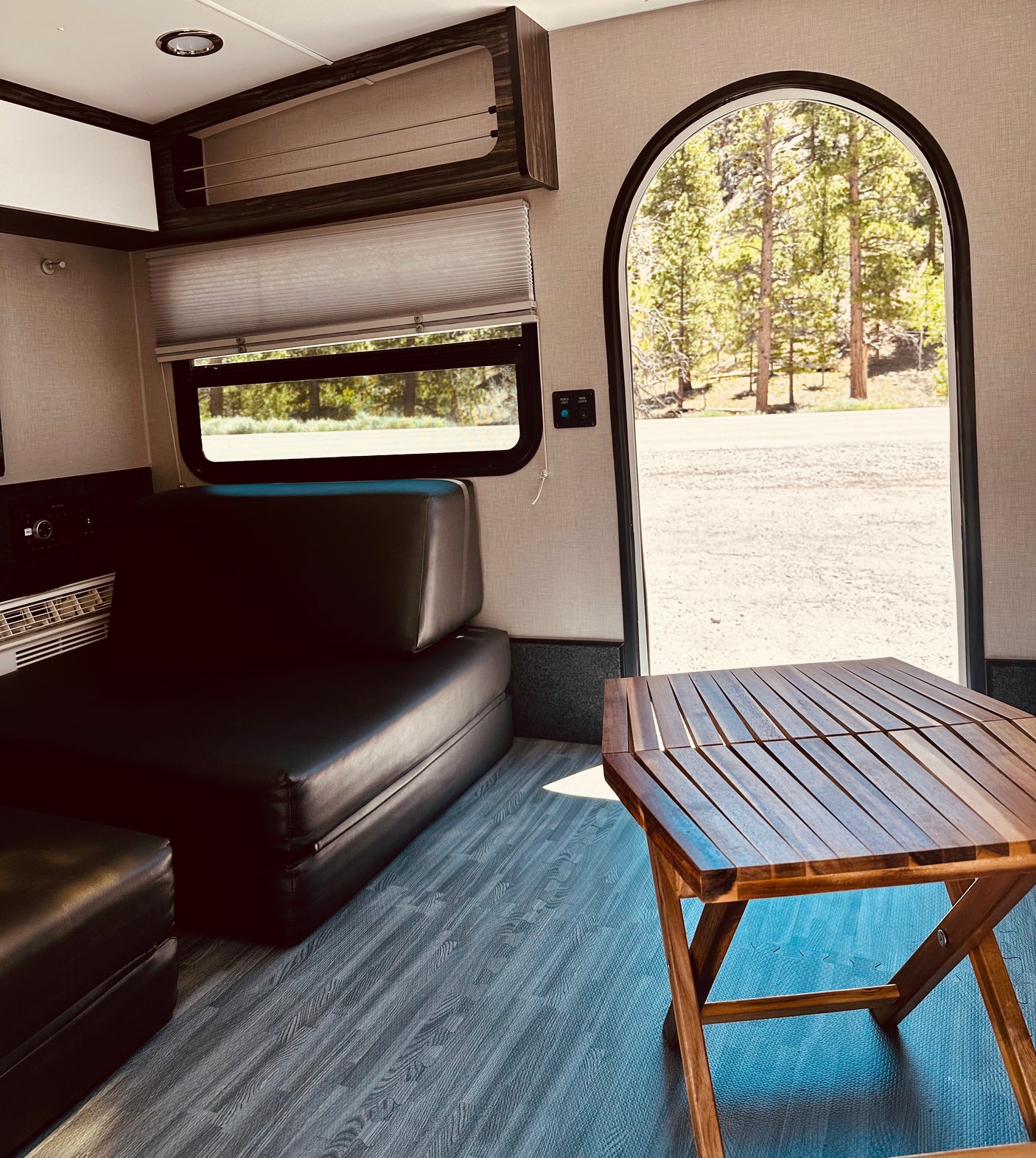 Interior of an RV rental featuring a dark couch, wooden portable table, and an arched doorway framing a forest view.