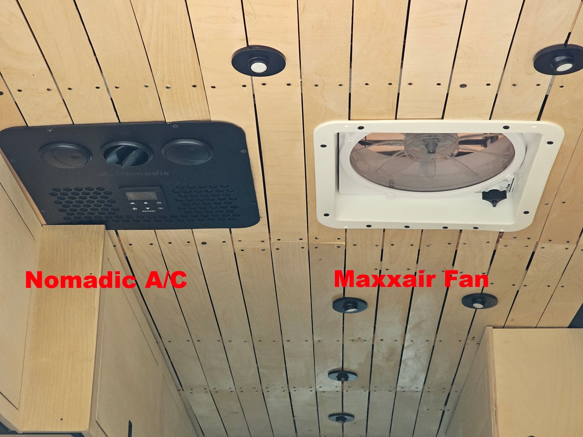 Ceiling view inside an RV rental, showing a black Nomadic A/C unit on the left and a white Maxxair Fan on the right, on light wood panels.