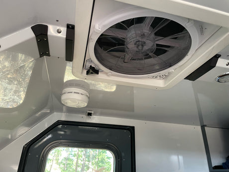 Inside an RV rental: a powerful ceiling fan, smoke detector, and window for comfort and safety on your travels.