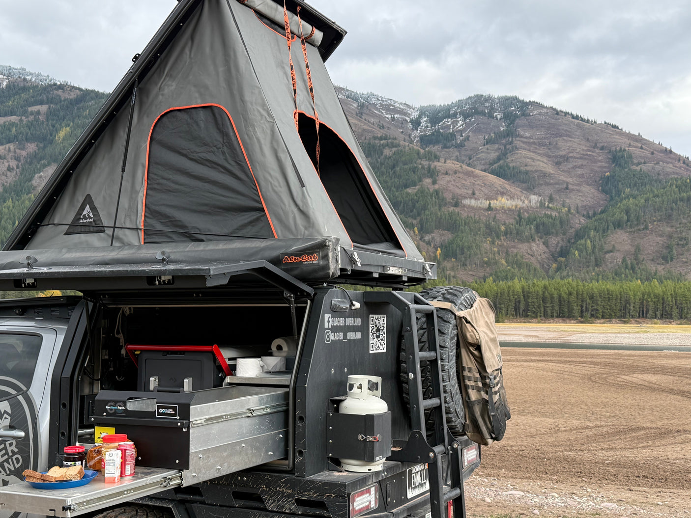 Glacier Overland's Alu-Cab rv rental: An overlanding truck with a rooftop tent and camp kitchen set up in the mountains.