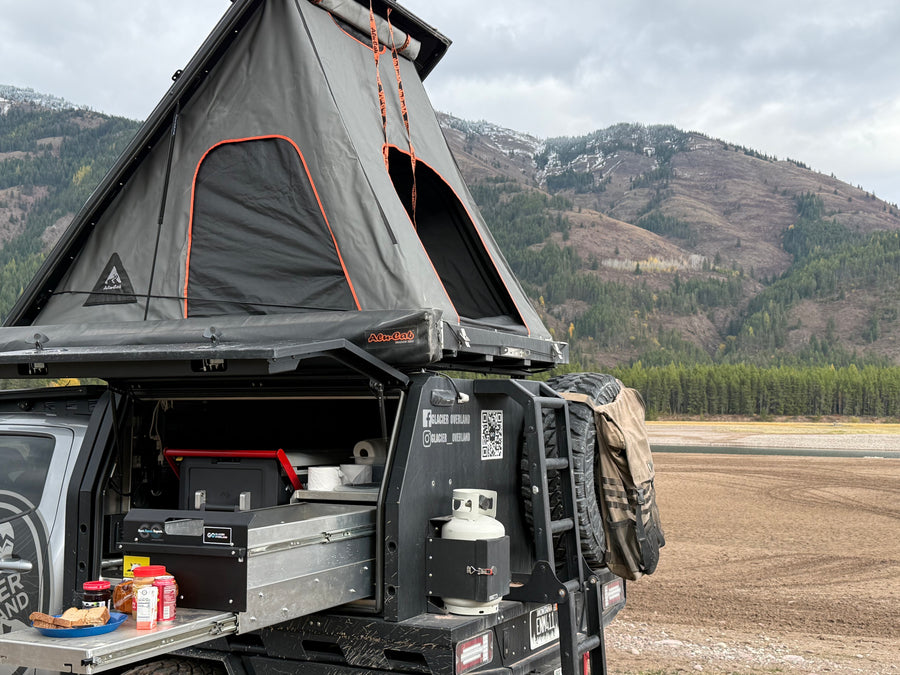 Glacier Overland's Alu-Cab rv rental: An overlanding truck with a rooftop tent and camp kitchen set up in the mountains.
