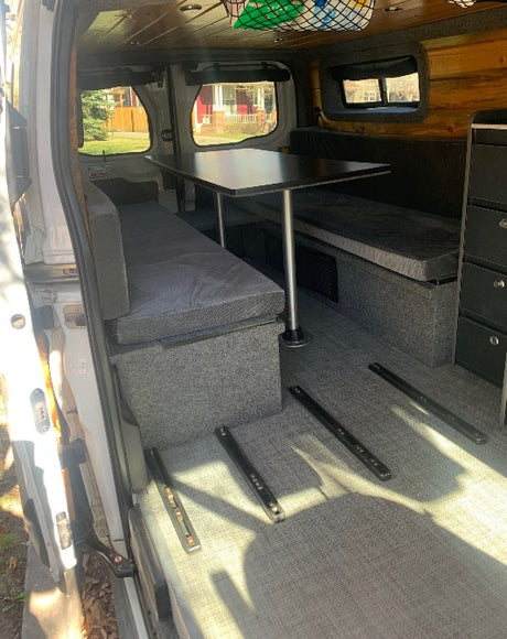 RV rental: Modular camper van interior with grey bench seating, table, floor tracks, and wood ceiling. Versatile for travel.