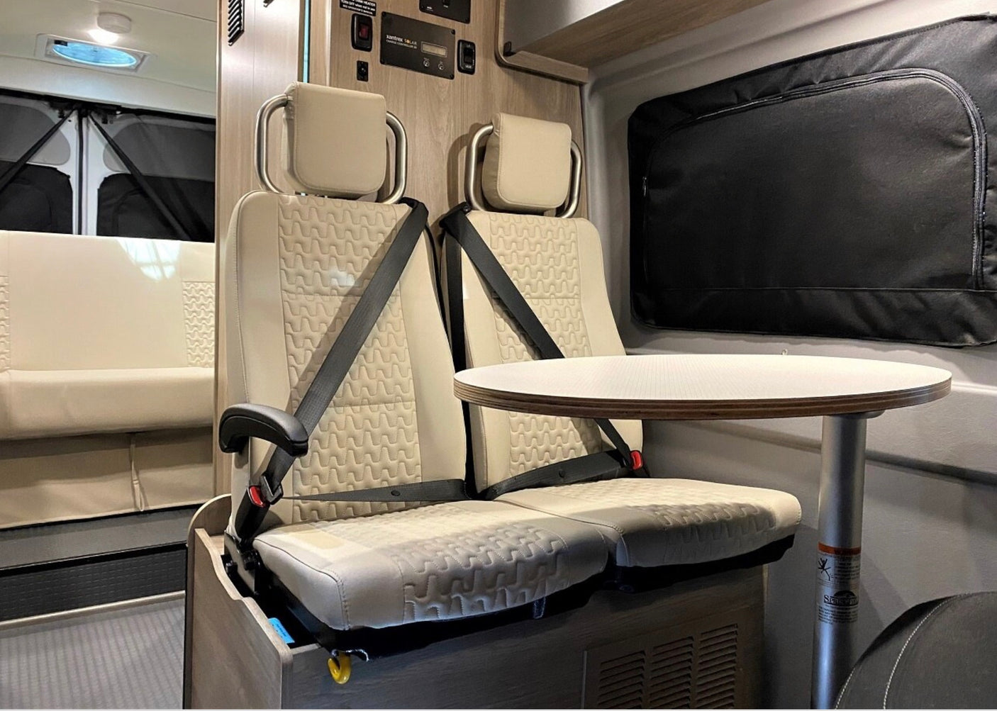Inside an RV rental: two beige passenger seats with seatbelts and a small dining table. Ready for comfortable travel.