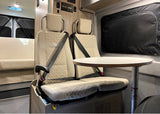 Inside an RV rental: two beige passenger seats with seatbelts and a small dining table. Ready for comfortable travel.