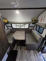 Compact RV rental interior featuring a cozy dinette with patterned cushions, a wood-look table, and large windows.