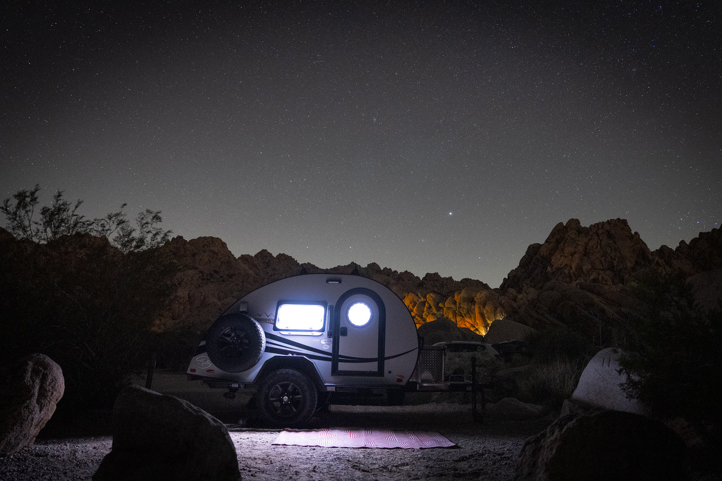An illuminated RV rental glows under a brilliant starry night sky. Perfect desert camping for stargazing among the rock formations.