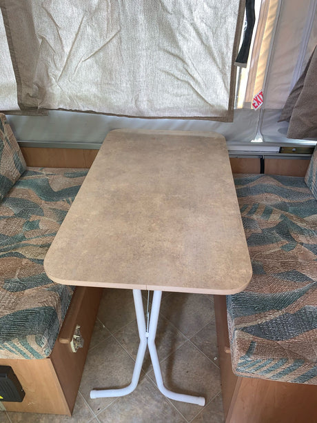 This RV rental's dinette features a removable table between two patterned bench seats, under canvas pop-up walls.