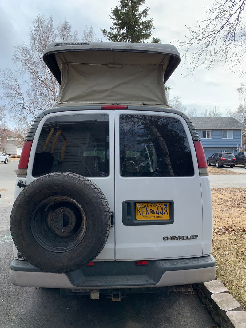 Rear view of a white Chevrolet Sportmobile pop-top camper van, an RV rental, with a spare tire and Alaska license plate. — photo 13