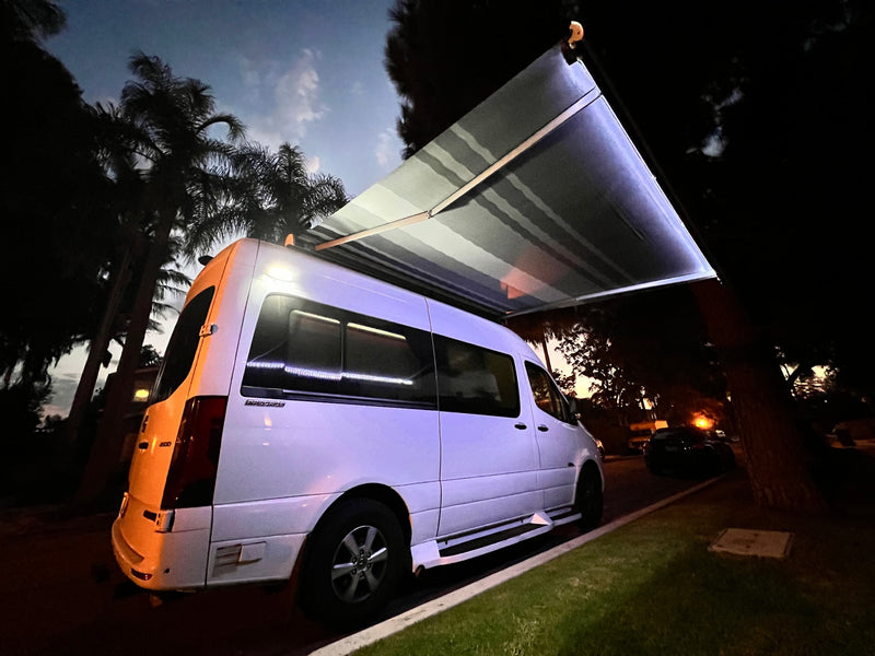 White camper van with an extended awning, parked at night under palm trees, perfect for your RV rental adventure. — photo 2