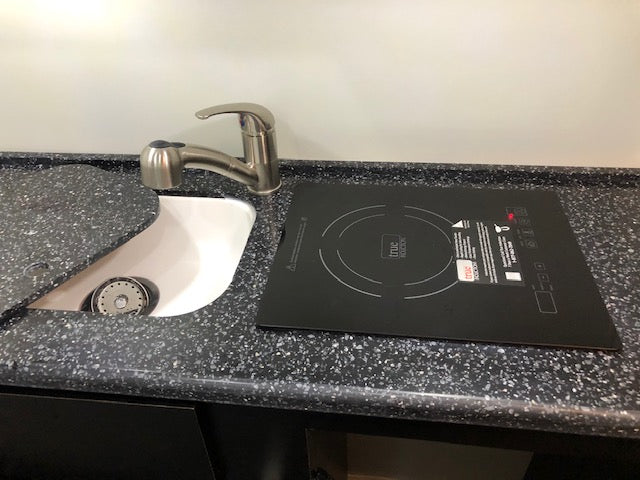 Compact RV rental kitchen counter with a small sink, pull-down faucet, and a black True Induction cooktop. Ideal for mobile living. — photo 11