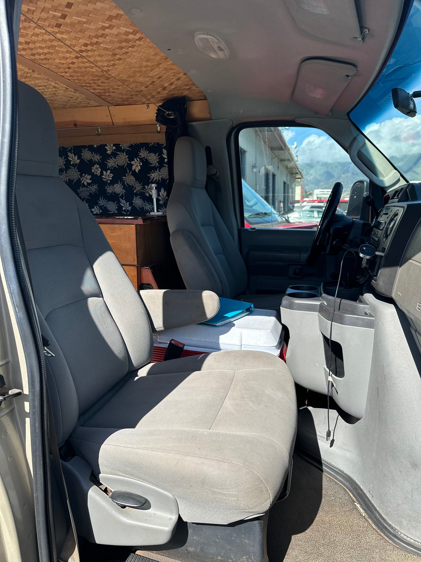 Inside a unique RV rental: front cabin with grey seats, a cooler, and a glimpse of the custom living space featuring a woven ceiling.