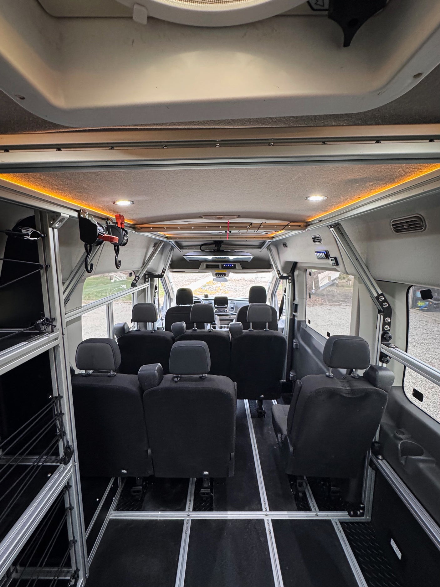 Spacious RV rental van interior featuring modular black seating on floor tracks, overhead lighting, and side storage for versatile travel.