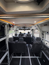 Spacious RV rental van interior featuring modular black seating on floor tracks, overhead lighting, and side storage for versatile travel.