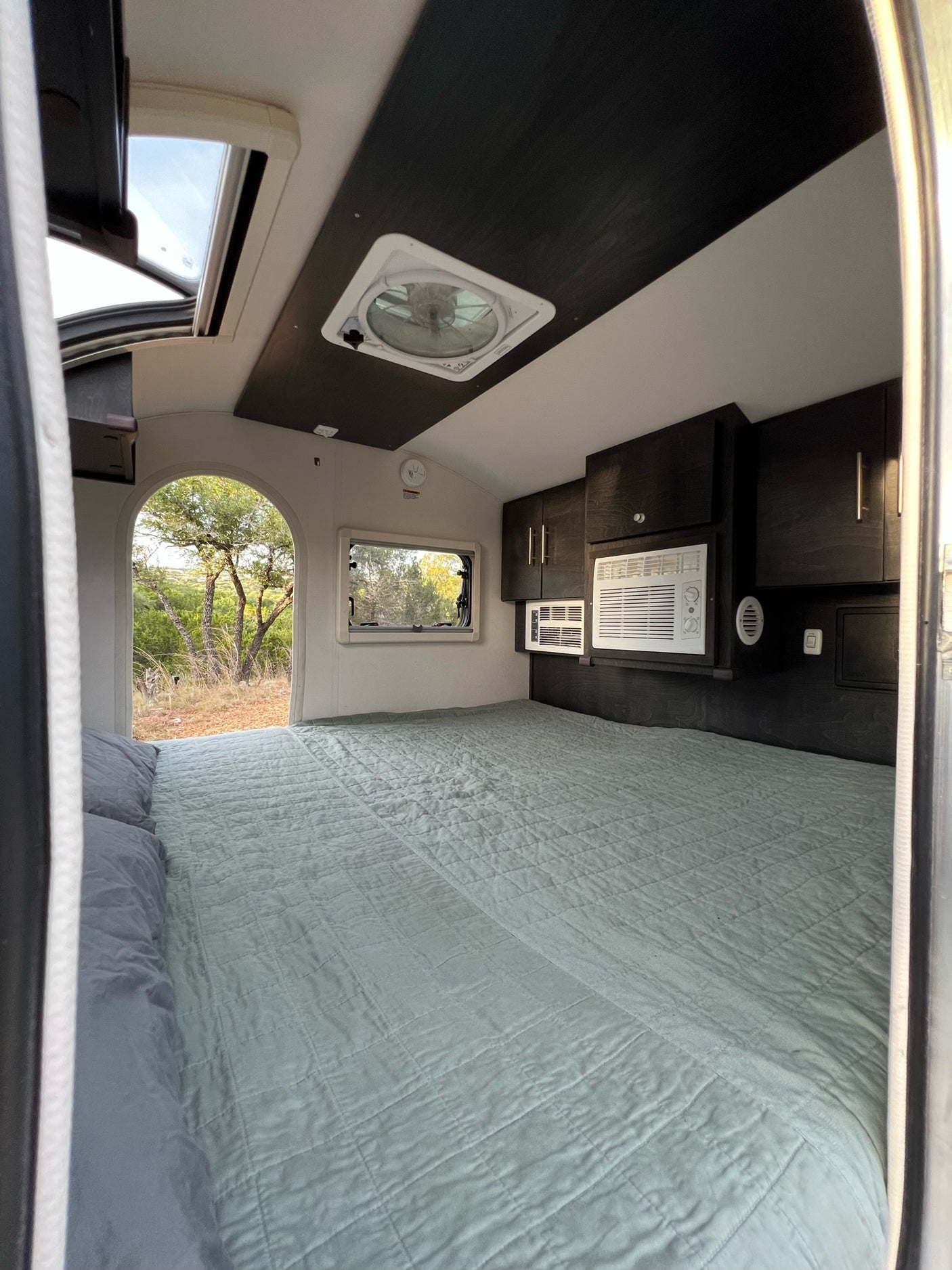 Inside a comfy RV rental bedroom featuring a spacious bed, AC units, and scenic outdoor views.